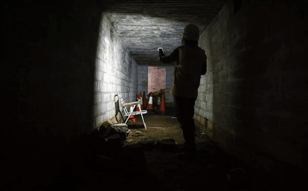 Строитель со смартфоном освещает темный коридор подземного бункера времен войны