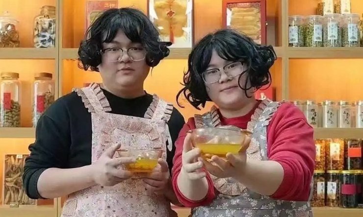 Чоловік і дружина з Китаю в перуках і однакових фартухах тримають миски з трав'яним настоєм