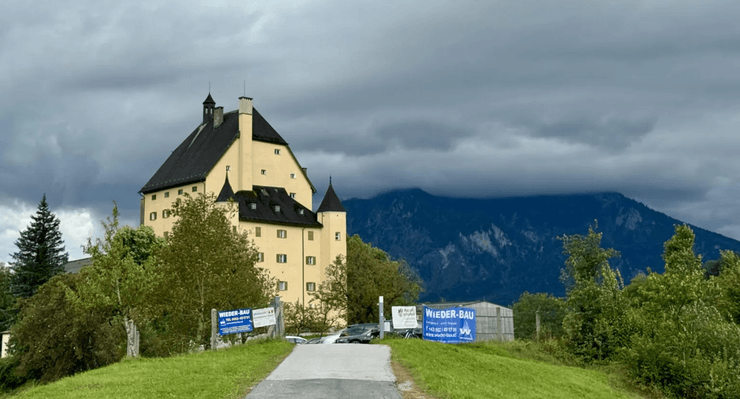 Желтое здание замка Голденштайн в Эльсбетене, Австрия, на фоне гор и пасмурного неба