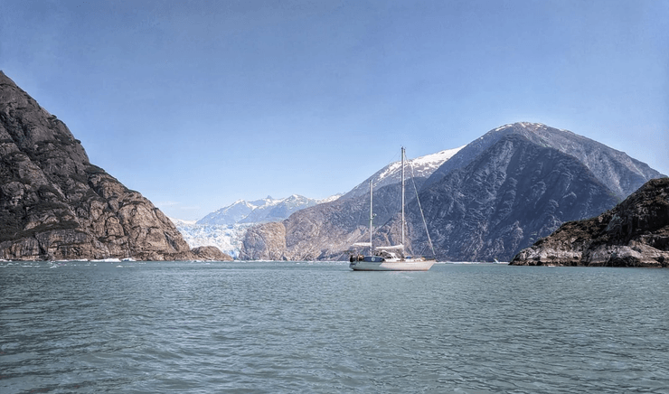 Белая яхта стоит на воде у ледников и горных склонов в Аляске