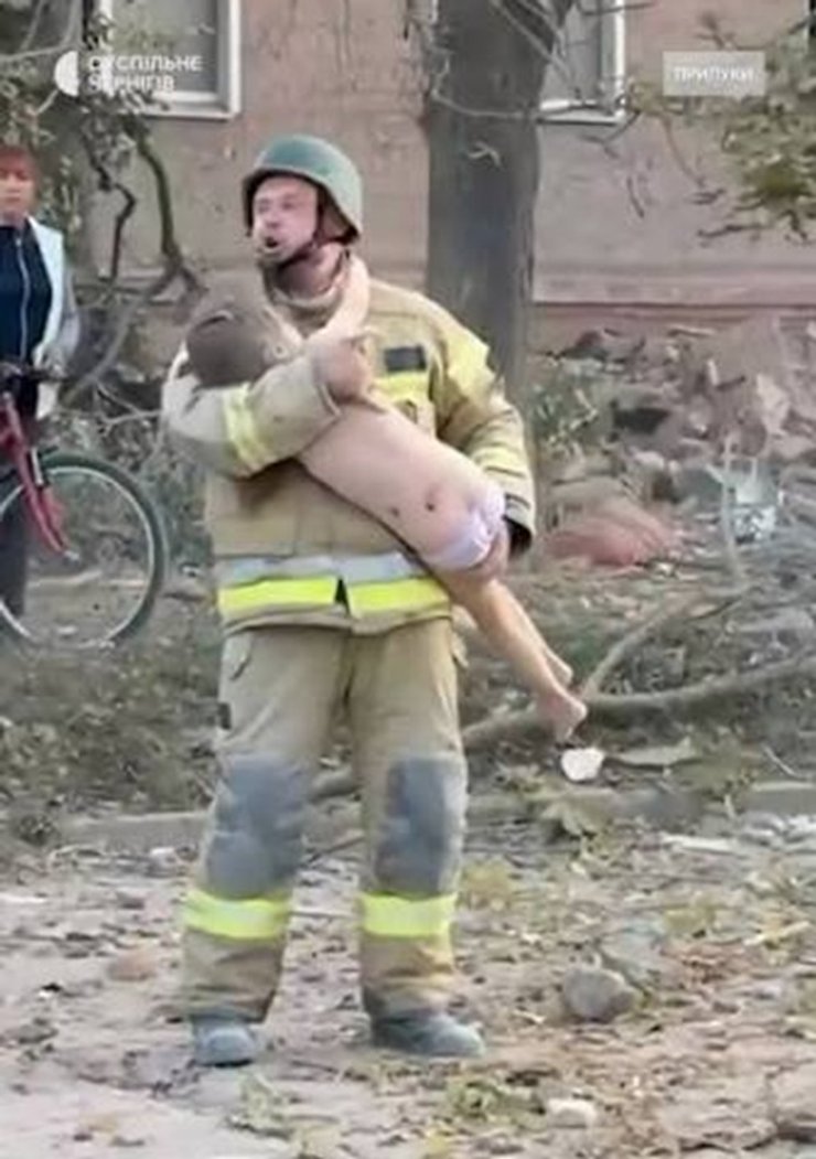 Рятувальник Павло Левченко несе врятовану дівчинку після удару по Прилуках Співробітник ДСНС Павло Левченко тримає на руках врятовану дівчинку на тлі зруйнованого будинку у Прилуках