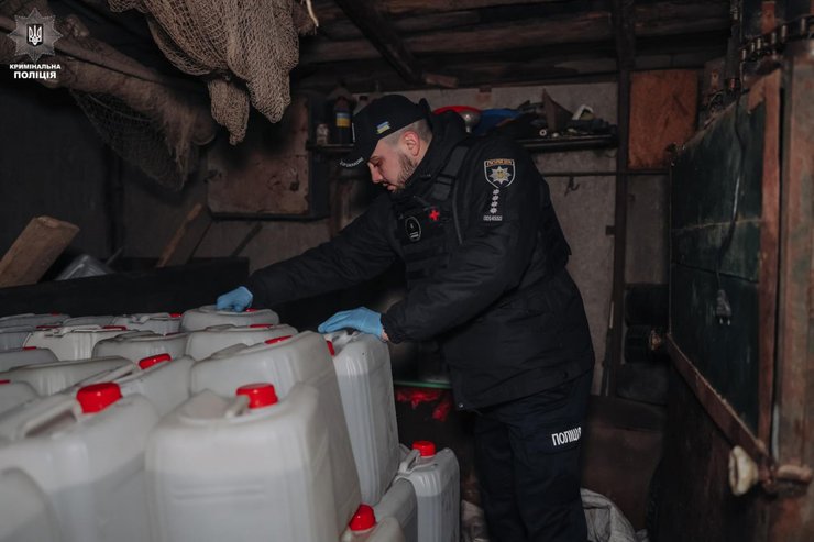 Сотрудник Национальной полиции Украины в перчатках осматривает многочисленные пластиковые канистры с красными крышками в складском помещении
