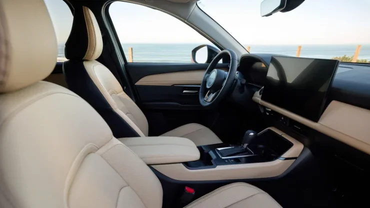 Салон кроссовера Mazda 2027 года со светлыми кожаными сиденьями и цифровым экраном мультимедиа на фоне моря