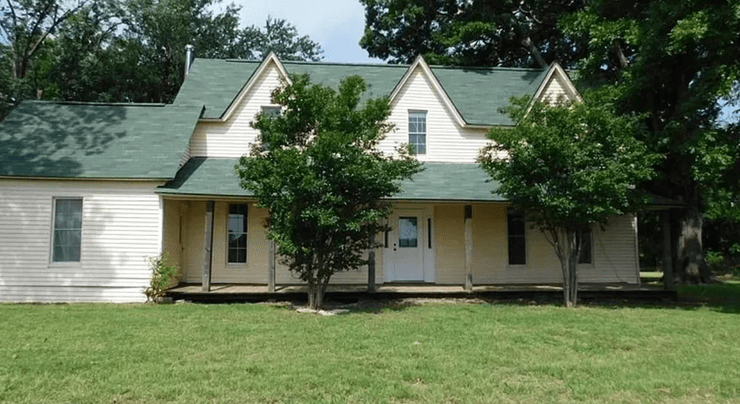 Фасад двоповерхового фермерського будинку із зеленим дахом і верандою, зруйнований торнадо