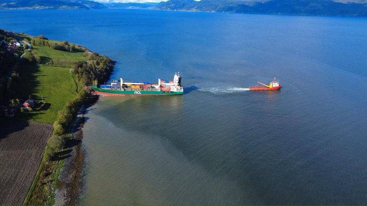 Вид с воздуха на контейнеровоз, севший на мель у берега Тронхеймского фьорда в Норвегии, рядом с жилыми домами