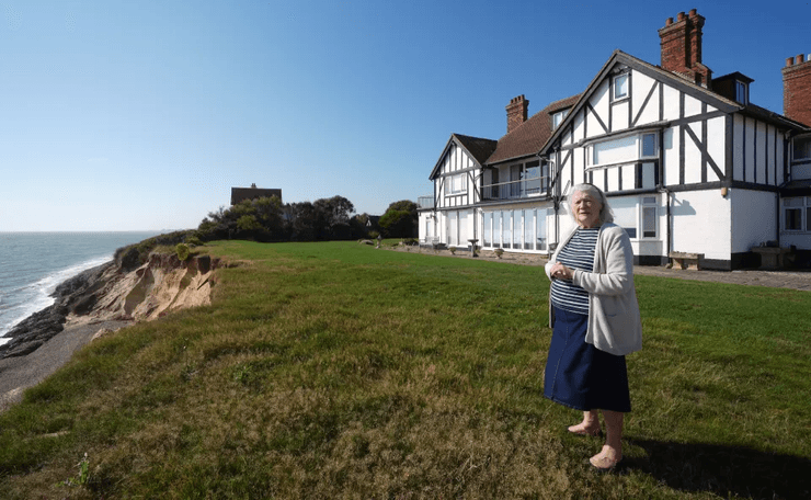 88-летняя женщина стоит у своего дома в Саффолке, рядом с обрывом, подточенным эрозией