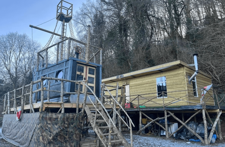 Будинок у формі піратського корабля і дерев'яна споруда на палях на березі річки в графстві Вустершир