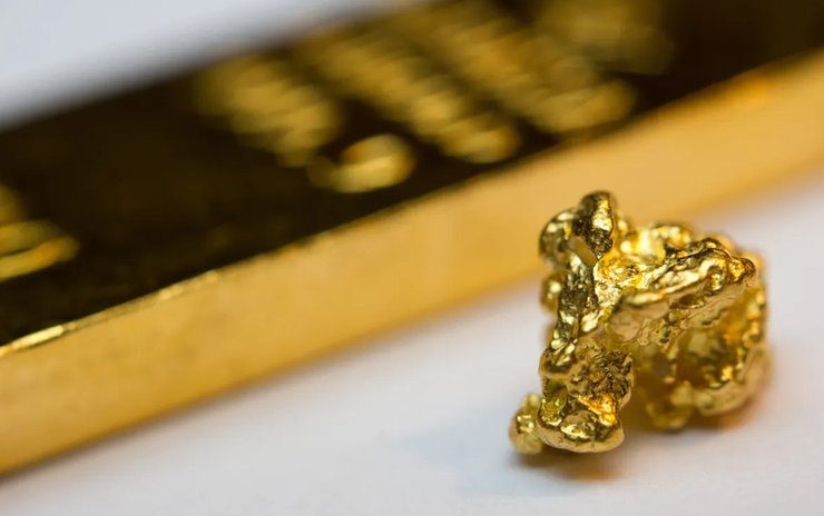 Золотой слиток и найденный самородок золота, лежащие на белой поверхности крупным планом