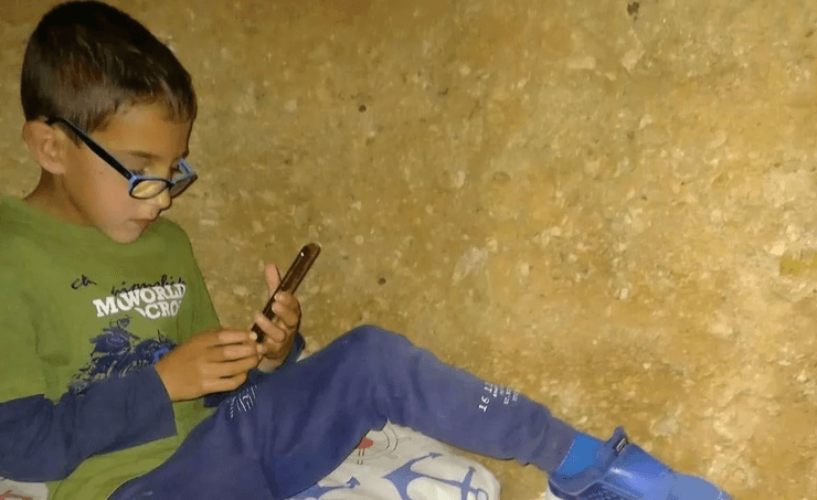 Хлопчик сидить у підземній камері і користується телефоном у тунелі, виритому в саду