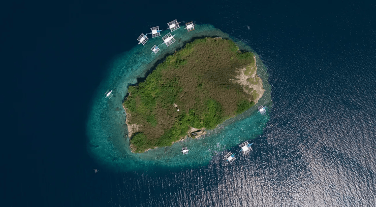 Вид с воздуха на зеленый остров в океане, окружённый лодками и рифами