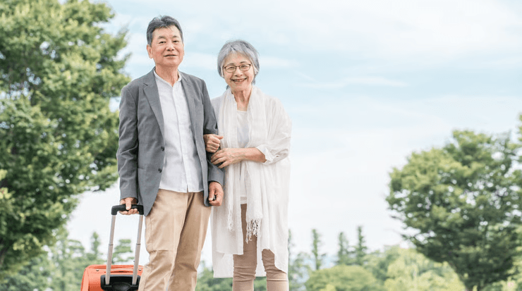 Чоловік і жінка похилого віку стоять разом на вулиці з валізою, усміхаючись