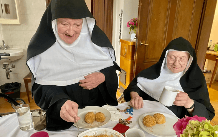 Пожилые монахини в черно-белых одеяниях сидят за столом и пьют чай в монастыре Голденштайн