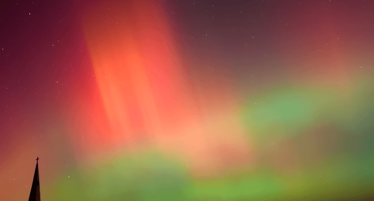 Червоні та зелені смуги північного сяйва, видимі над силуетом церкви на нічному небі