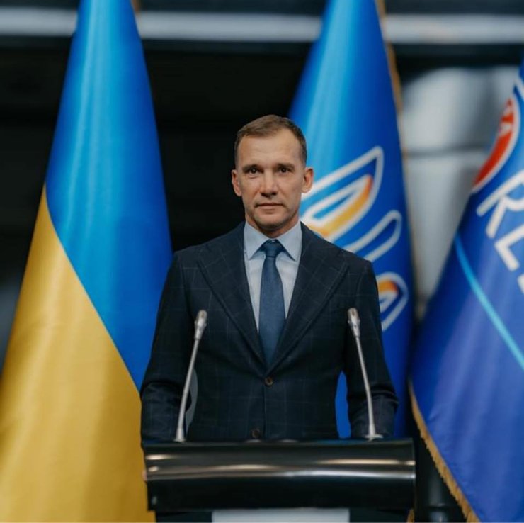 Андрей Шевченко за трибуной на фоне флагов Украины и УАФ
