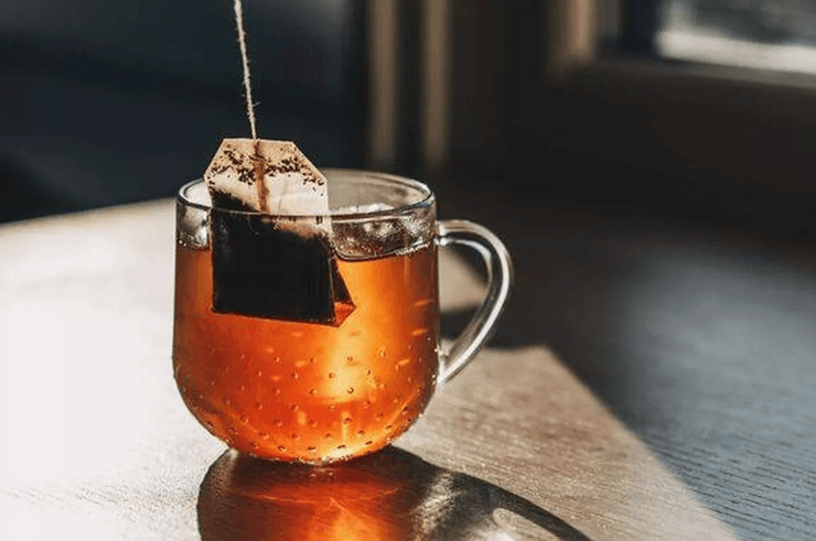 Чайний пакетик у прозорому кухлі з чаєм, люди сильно вичавлюють чайний пакетик