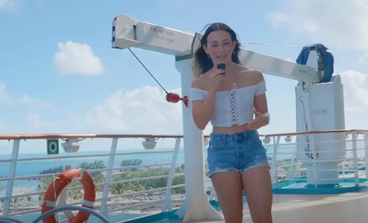 Дівчина в білому топі та джинсових шортах стоїть на палубі круїзного лайнера Liberty of the Seas