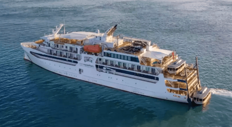 Белый круизный лайнер Coral Adventurer компании Coral Expeditions, идущий по морю при спокойной погоде