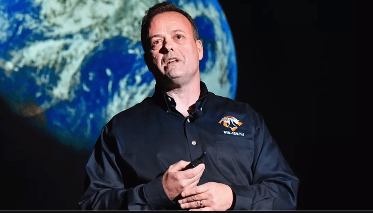 Астронавт выступает с лекцией о восприятии Земли из космоса на фоне изображения планеты