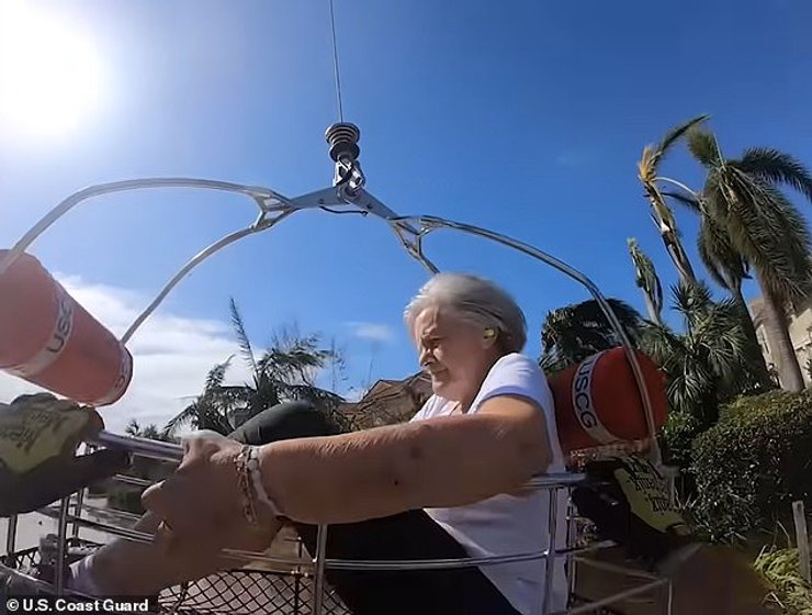 Женщину поднимают на вертолете в корзине.