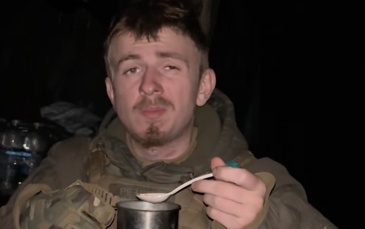 Військовослужбовець дегустує гарячу страву з армійського сухпайка в польових умовах під час нічного дозору