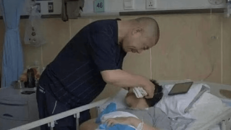 Мъж се навежда над болнично легло, бършейки лицето на болна жена в медицинско отделение