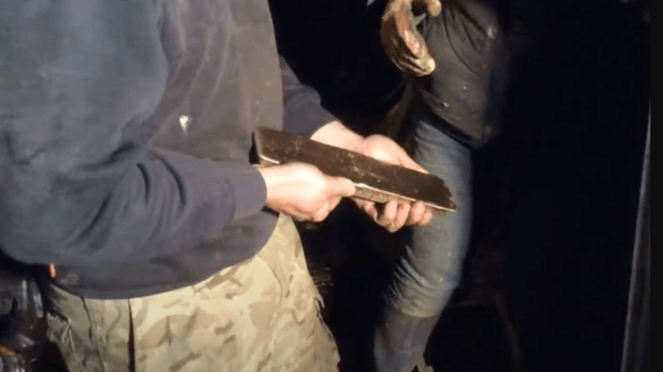 Мужчина держит в руках золотой слиток, обнаруженный при осмотре военной техники