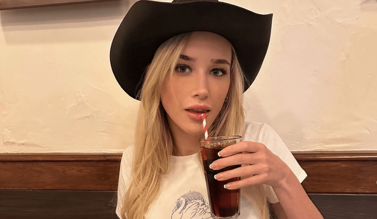 Блондинка в черной ковбойской шляпе пьёт газированный напиток через трубочку