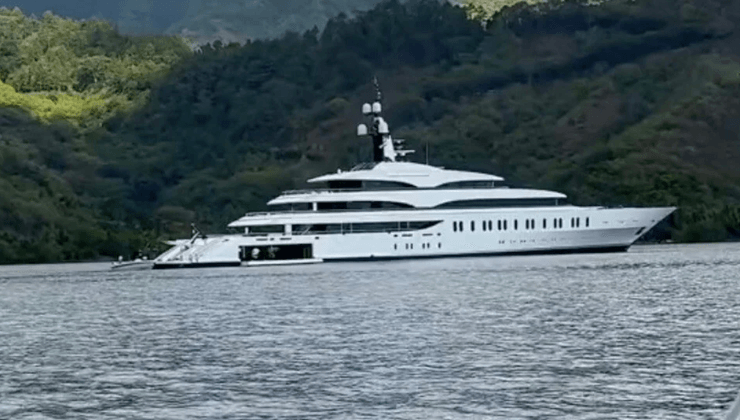 Мегаяхта IJE, принадлежащая миллиардеру, стоит у берегов тропического острова на фоне зеленых холмов
