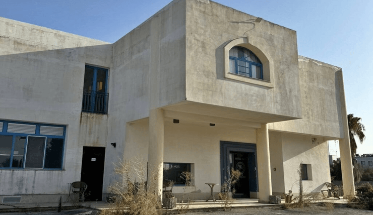 Старинное здание заброшенного отеля с выгоревшими стенами, закрытыми окнами и заросшей территорией перед входом