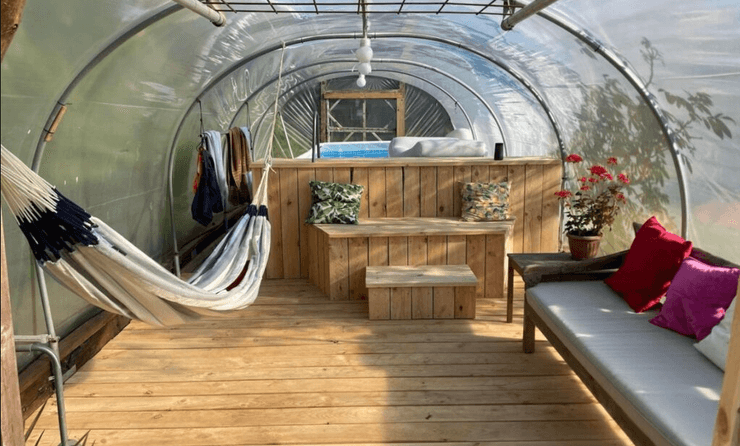 Зона отдыха в теплице с гамаком, деревянной мебелью и небольшим бассейном в доме, который пара предлагает для обмена