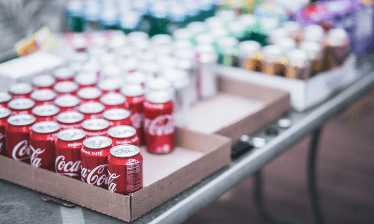Червоні алюмінієві банки Coca-Cola, викладені в коробці серед інших напоїв