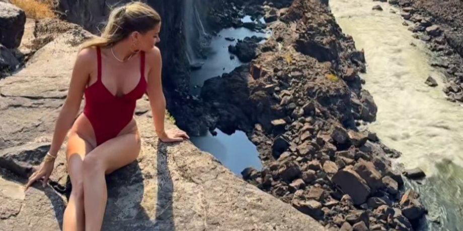 Женщина в красном купальнике сидит на краю скалы у водопада Виктория, не подозревая, что за ее спиной ползает змея