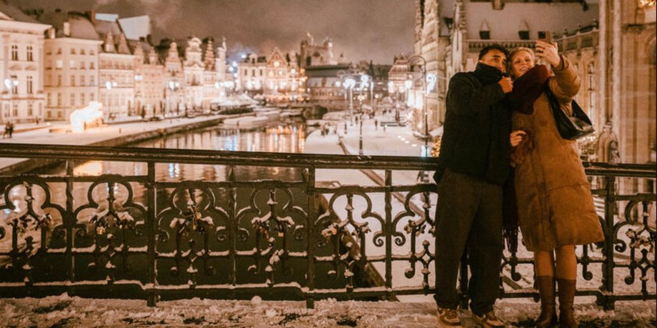 Пара фотографується на мосту в зимовому Генті з різдвяними вогнями і каналом на тлі