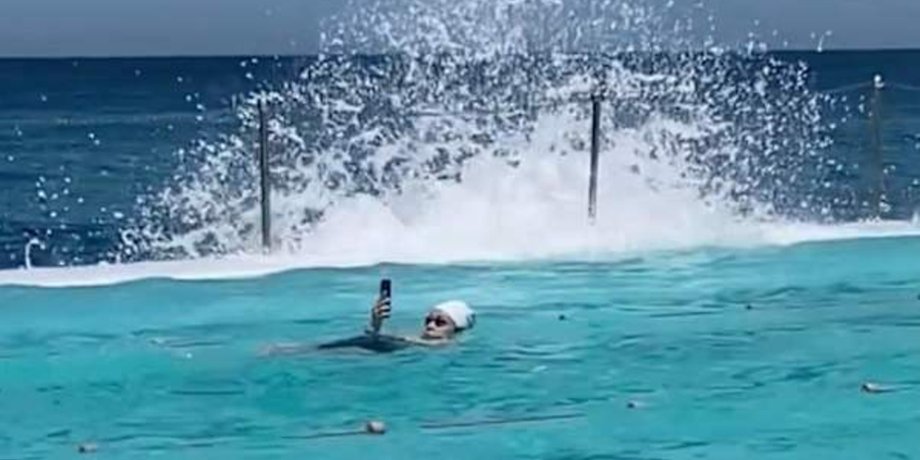 Женщина в шапочке плавает в бассейне Bondi Icebergs в Сиднее, держа телефон над водой
