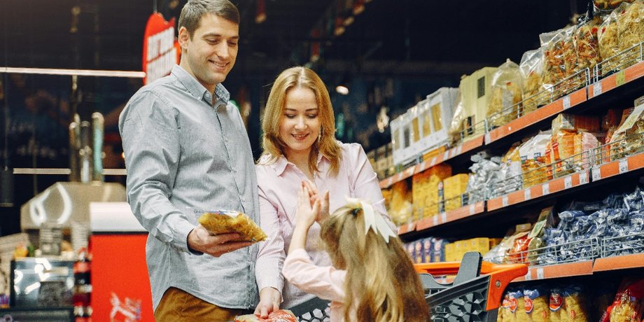 Отец, мать и дочь у стеллажа с продуктами в супермаркете