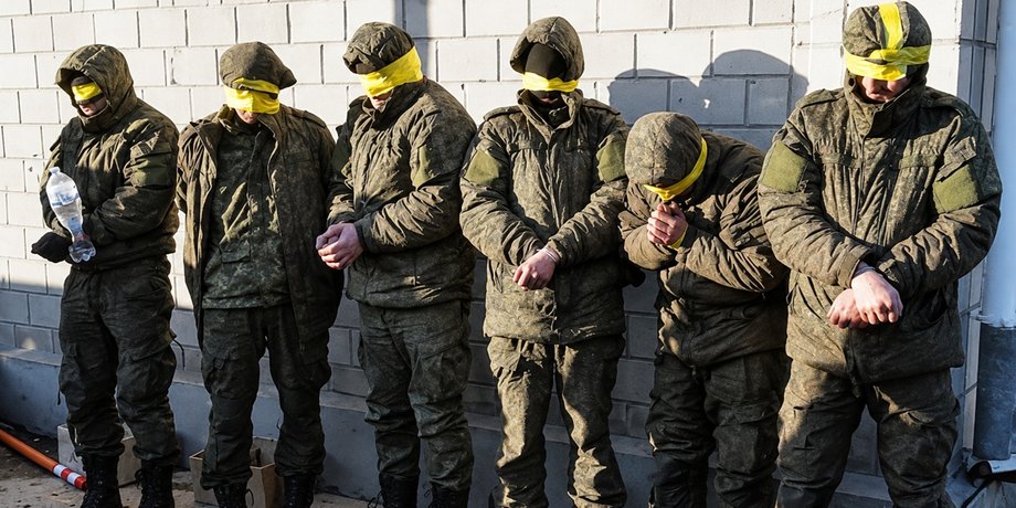 Полонені українці із зав’язаними очима стоять біля стіни під наглядом охорони