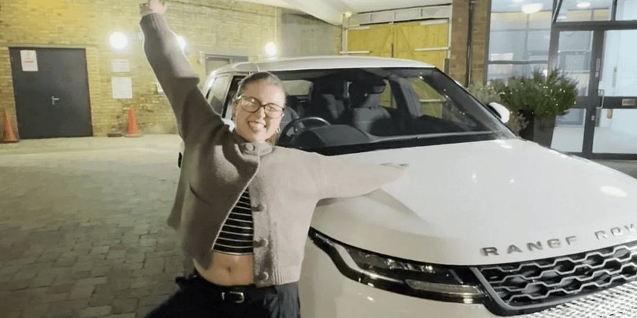 Девушка позирует рядом с белым Range Rover после победы в корпоративном рождественском розыгрыше
