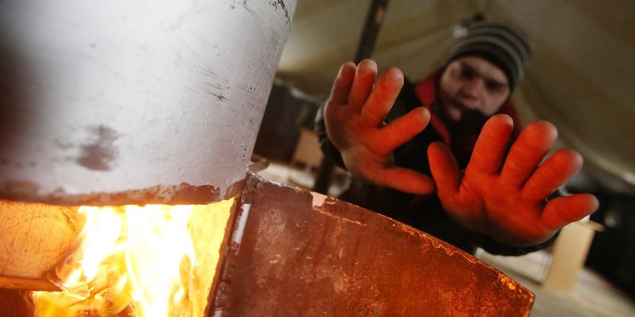 Чоловік гріється біля пічки під час відключення опалення у Києві