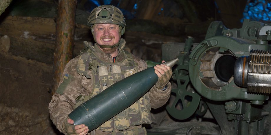 Артиллерист со снарядом и пушкой на позиции