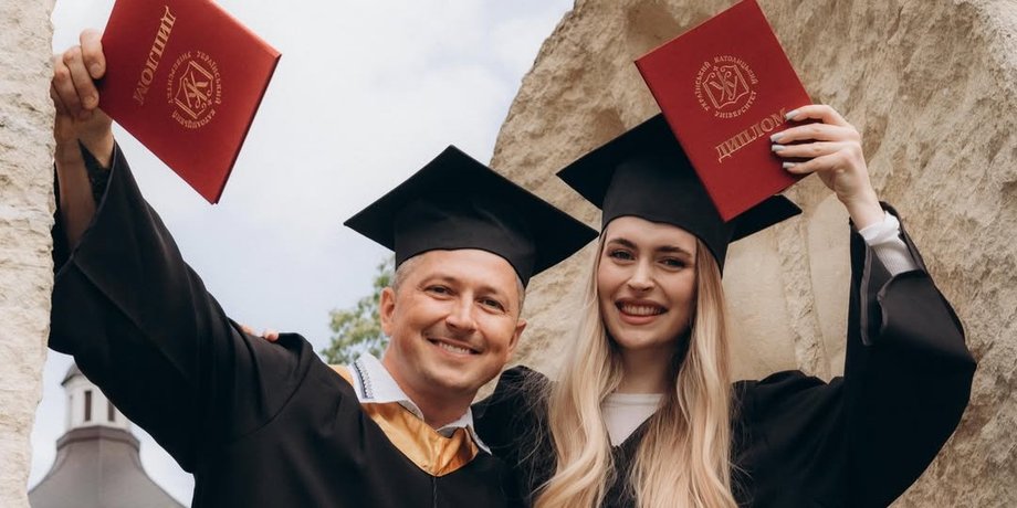 Український телеведучий Олександр Педан та його донька Валерія в чорних академічних мантіях і конфедератках посміхаються та тримають у руках червоні дипломи випускників
