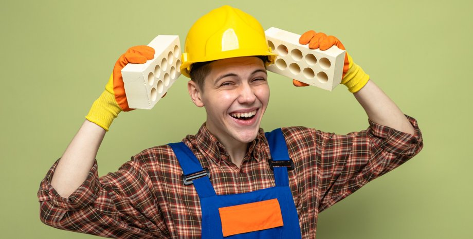 Будівельник усміхається і тримає цеглу
