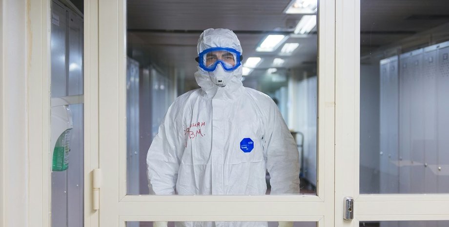 Людина в захисному костюмі Медик у білому захисному костюмі за дверима