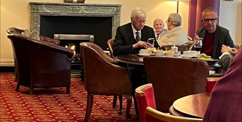 Пожилые мужчины сидят за столиком в ресторане Атенеума в Ливерпуле, разговаривают и пользуются телефоном