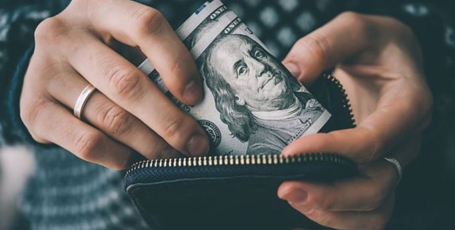 Людина ховає готівку у доларах в гаманець