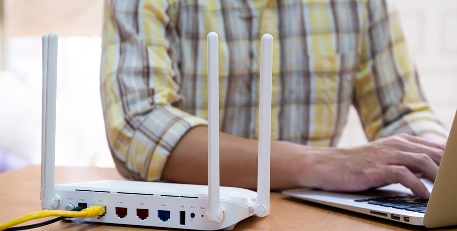 Чоловік працює з ноутбуком перед роутером Wi-Fi