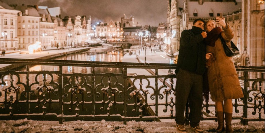 Пара фотографируется на мосту в зимнем Генте с рождественными огнями и каналом на фоне