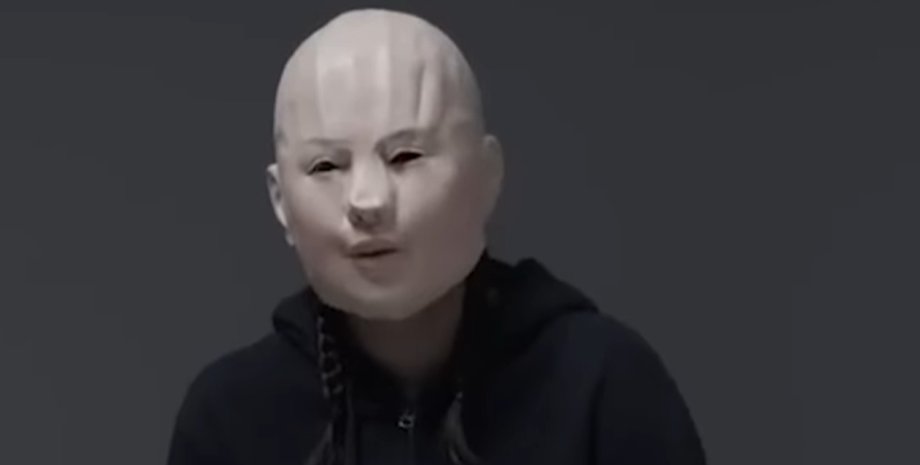 Жінка у світлій масці та темному одязі дає інтерв'ю, приховуючи обличчя