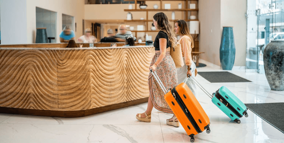 Две девушки с чемоданами заселяются в гостиницу, подходя к стойке регистрации