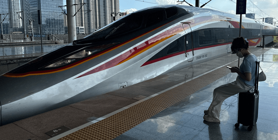 Пасажирка сидить на валізі на пероні поруч із високошвидкісним китайським поїздом на сучасному вокзалі