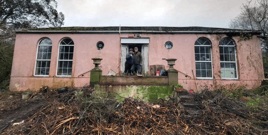 Подружня пара стоїть біля входу в рожевий будинок, куплений на аукціоні без попереднього огляду